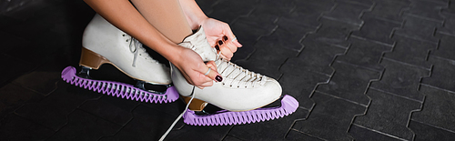 cropped view of young woman tying figure skating shoes, banner