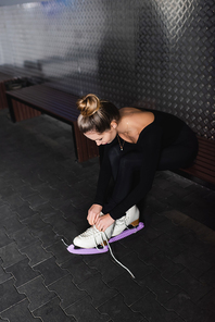 young woman tying figure skating shoes while sitting on bench