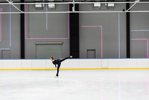 side view of young woman in black bodysuit skating in professional ice arena