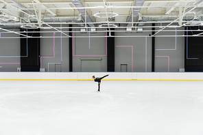 side view of figure skater in black bodysuit skating in professional ice arena