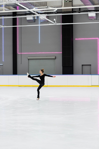 full length of figure skater in black bodysuit practicing in professional ice arena
