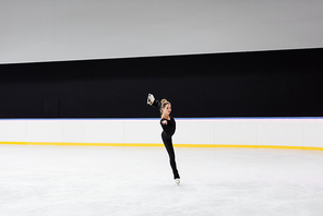 full length of figure skater in black bodysuit skating in frozen ice arena