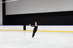 full length of woman in black bodysuit practicing in professional ice arena