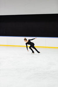 full length of professional figure skater in black bodysuit skating in ice arena