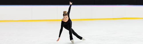 full length of professional figure skater in black bodysuit skating with outstretched hands in ice arena, banner