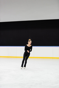 full length of cheerful professional figure skater in black bodysuit skating in ice arena