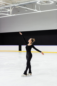 full length of sensual figure skater in black bodysuit skating with outstretched hands in ice arena