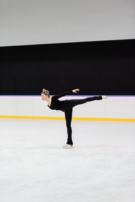 full length of professional figure skater in black bodysuit skating with outstretched hand in frozen ice arena