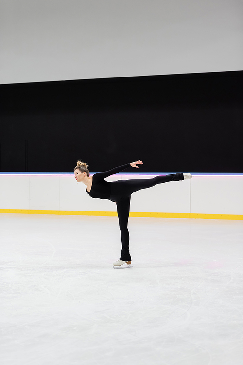 full length of professional figure skater in black bodysuit skating with outstretched hand in frozen ice arena