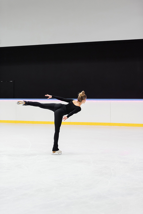 back view of professional figure skater in black bodysuit skating with outstretched hand in ice arena