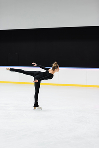 side view of professional figure skater in black bodysuit skating with outstretched hand in ice rink