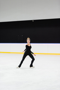 full length of professional figure skater in bodysuit skating in ice arena