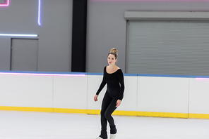 full length of young figure skater in black bodysuit skating in ice rink