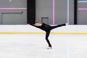 full length of young figure skater in black bodysuit skating with outstretched hand in ice arena
