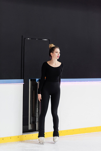 full length of young figure skater in bodysuit standing on frozen ice arena