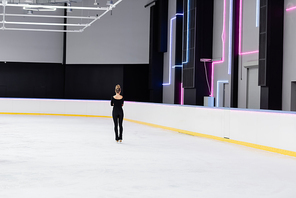 back view of young figure skater in black bodysuit and ice skates on frozen ice arena