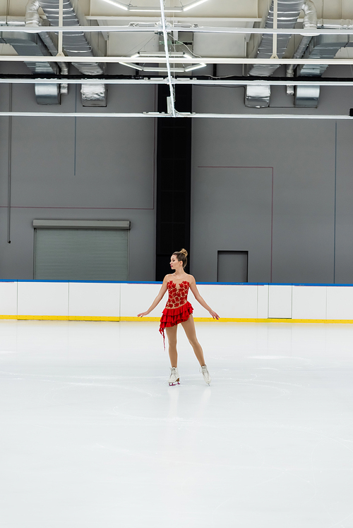 full length of young figure skater in dress performing dance in professional ice arena