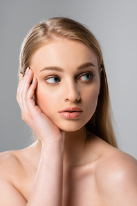 young woman touching face and looking away isolated on grey