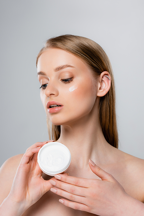 pretty woman with blue eyes holding container with face cream isolated on grey