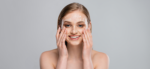 positive young woman with blue eyes applying cleansing foam on face isolated on grey, banner