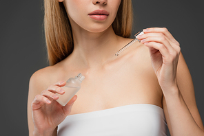 cropped view of young woman in white top holding cosmetic serum isolated on grey