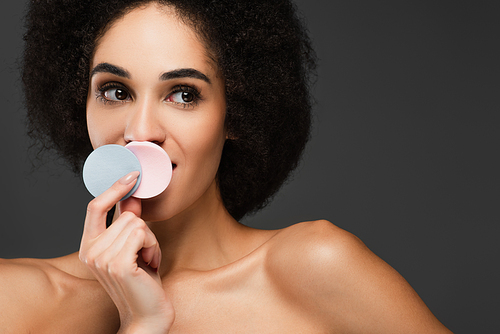 young african american woman holding cosmetic sponges near mouth isolated on grey