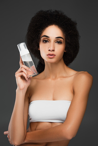 pretty african american woman in white top  while holding makeup remover isolated on grey
