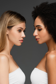 young multiethnic women with natural makeup standing face to face isolated on grey