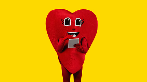person in red heart costume holding digital tablet isolated on yellow