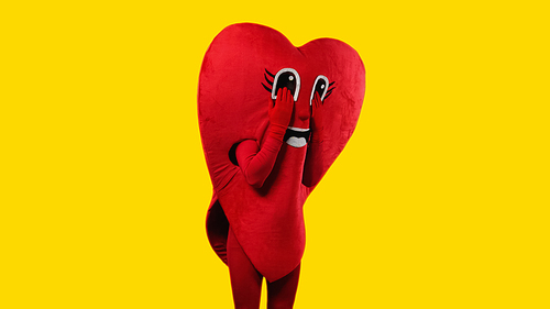 sad person in heart costume touching cartoon eyes while imitating crying isolated on yellow