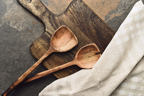 top view of wooden cutting board with spatulas and napkin on weathered background