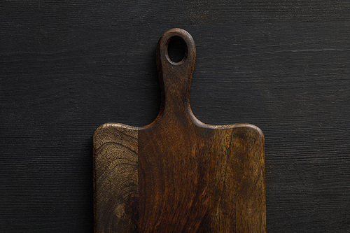 Top view of brown wooden cutting board on dark surface