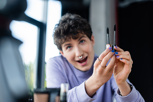Mascara brushes in hands of blurred transgender person near digital camera