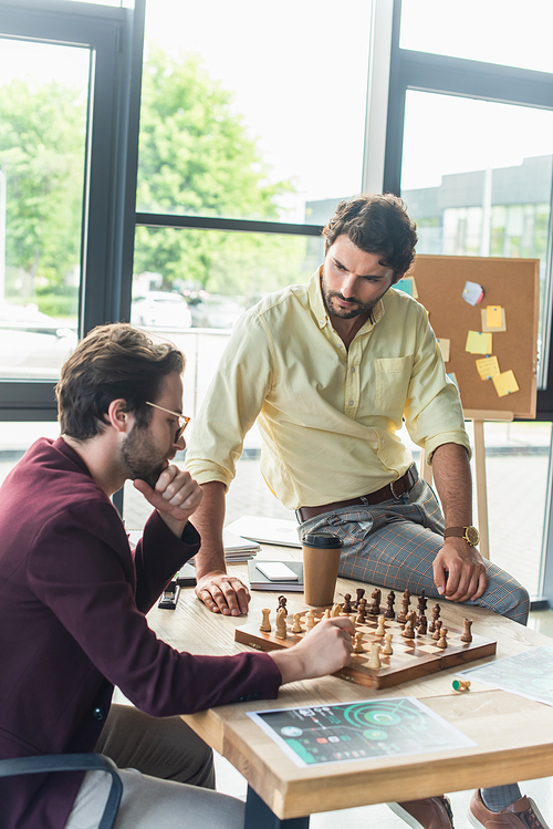 Business people in formal wear playing chess near papers in office