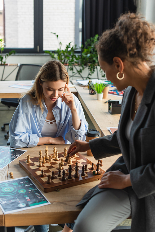 Pensive businesswoman looking at chess on board while playing with african american colleague in office