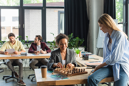 Positive african american businesswoman playing chess with colleague in office