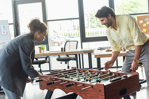 Side view of interracial business people playing table football in office