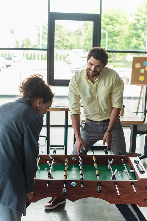 Smiling businessman playing table soccer with african american colleague in office