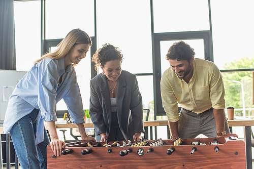 Cheerful multiethnic business people playing table soccer in office