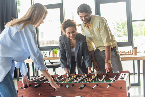 Positive interracial business people having fun while playing table soccer in office