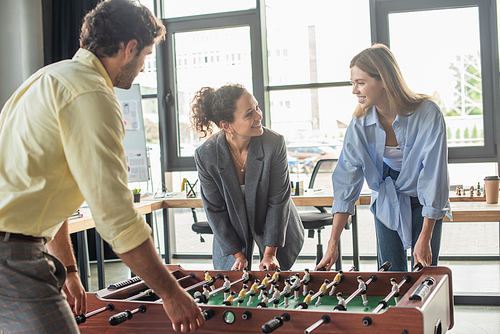 Smiling business people playing table soccer with african american colleage in office