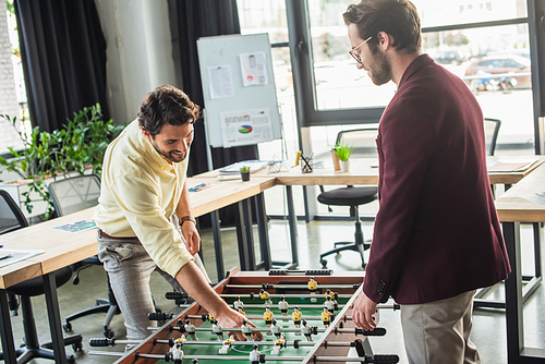 Positive businessman in formal wear playing table football in office