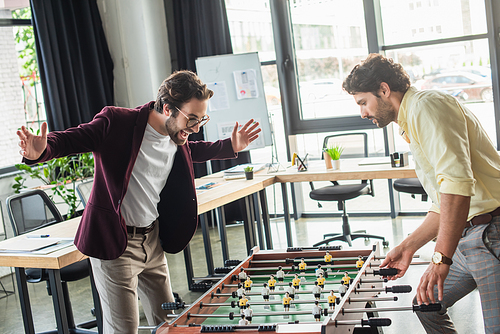 Excited businessman playing table soccer with colleague in office