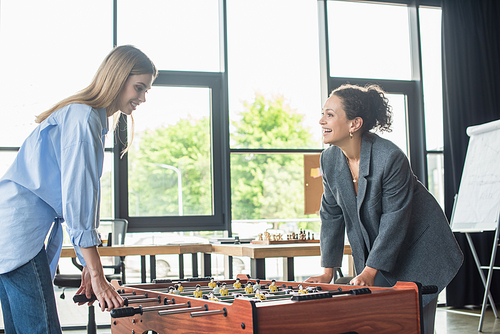 Cheerful african american businesswoman playing table soccer with colleague in office