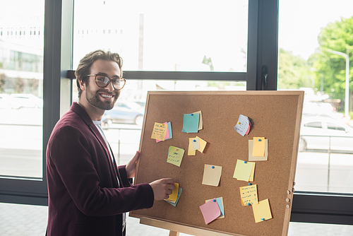 Positive businessman in eyeglasses  near board with sticky notes