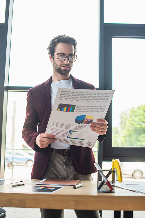 Young businessman holding document near working table in office