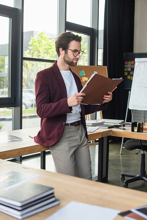 Young businessman looking at paper folder near table in office