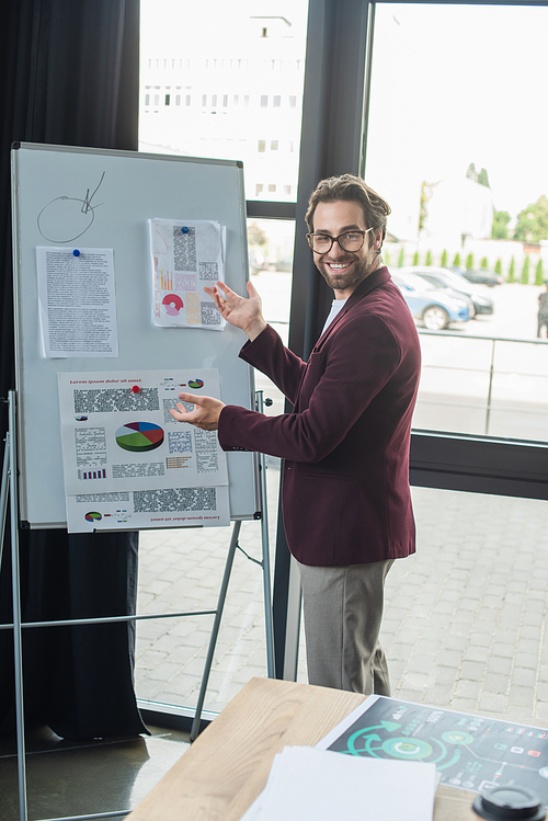 Smiling businessman pointing at charts on flipchart in office