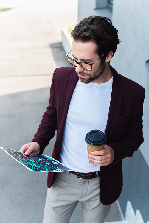 Young businessman holding coffee to go and document outdoors