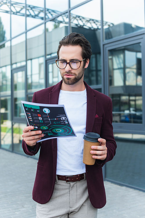 Young businessman in eyeglasses holding takeaway drink and paper with charts outdoors